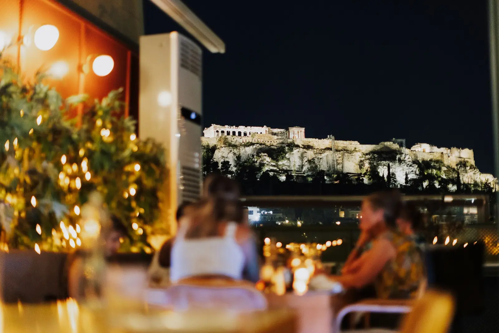 A candlelit rooftop dinner at night, the Acropolis lit up beyond it